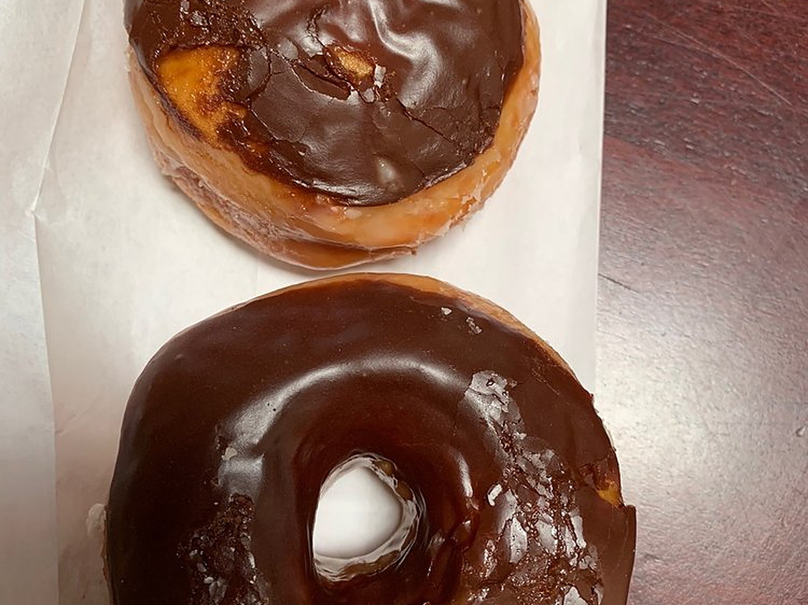 Chocolate glazed, still shining — two on the paper, chocolate over the glaze